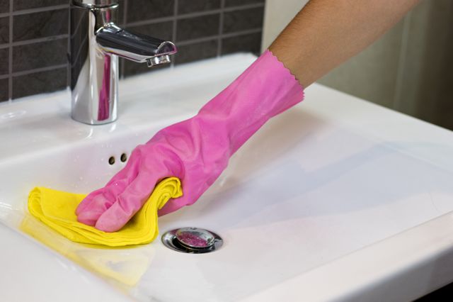 Hand in a pink glove and yellow cloth cleaning a sink | House Cleaning Omaha